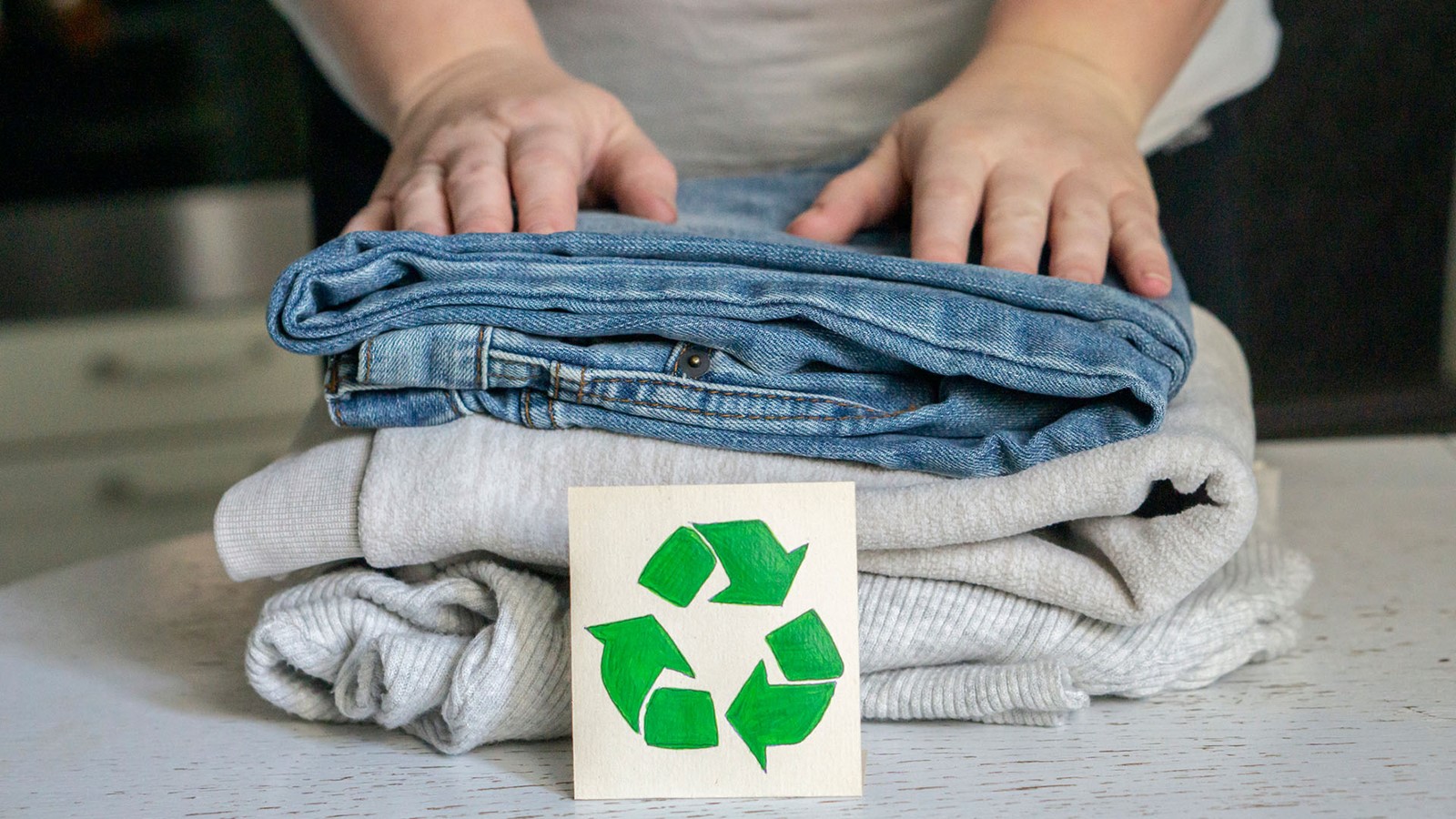 Bilde av noen klær brettet med et resirkuleringsskilt i forkant.