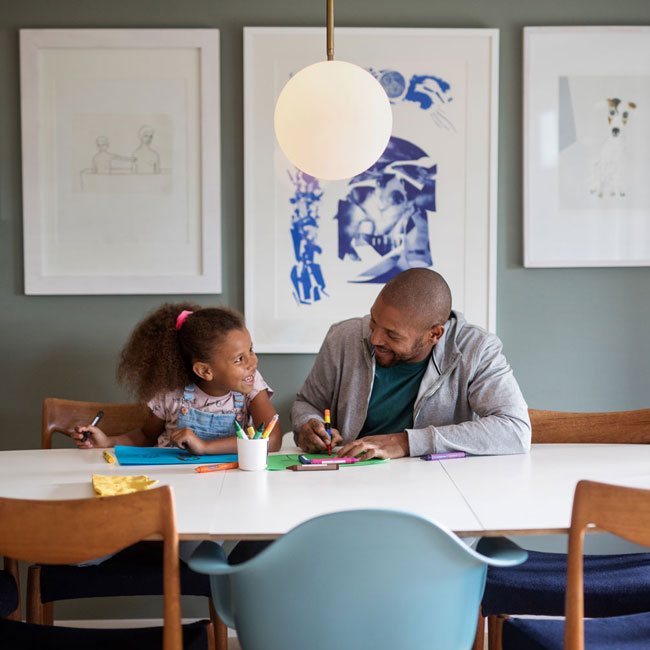 En far og datter som sitter ved et spisebord og tegner.