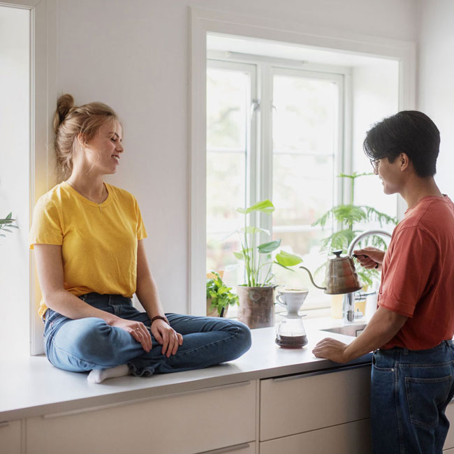 Usbl Hva er forkjøpsrett. Bilde av et ungt par som lager kaffe på kjøkkenet. Kvinnen sitter på kjøkkenbenken.