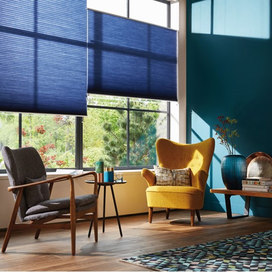 En stue med 2 lenestoler, mørkegrønne vegger og blå gardiner. Lys kommer inn gjennom vinduene.
