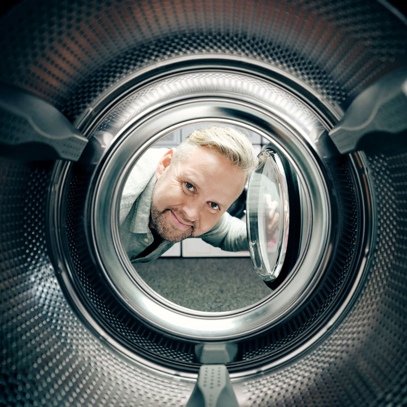 Man fra Skousen hvitevarer som ser inni en vaskemaskin og smiler.