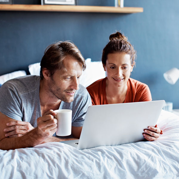En mann og en kvinner ligger på en seng mens de lese om Usbl strøm på en laptop PC.